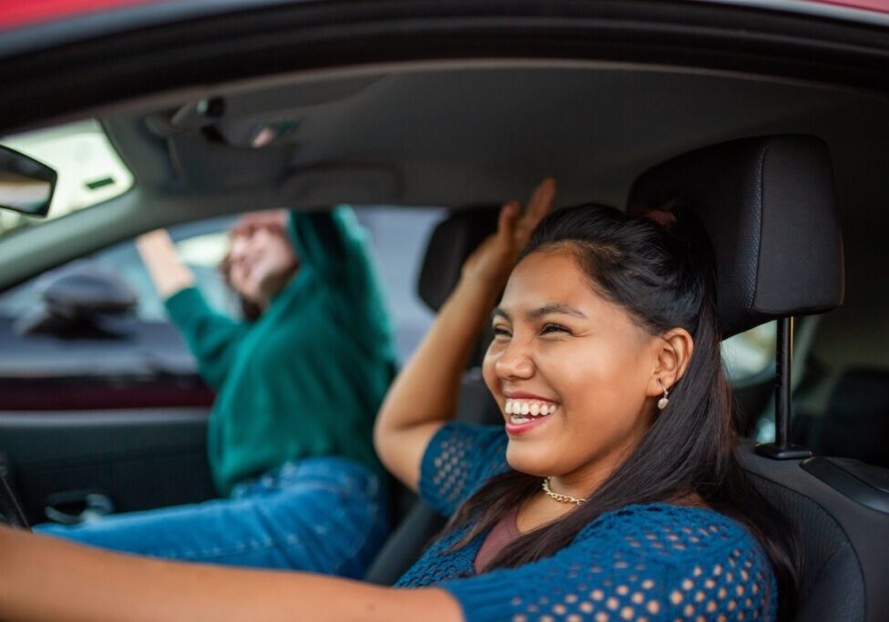 Two women laughing and celebrating while sitting in a red car gettingapproved